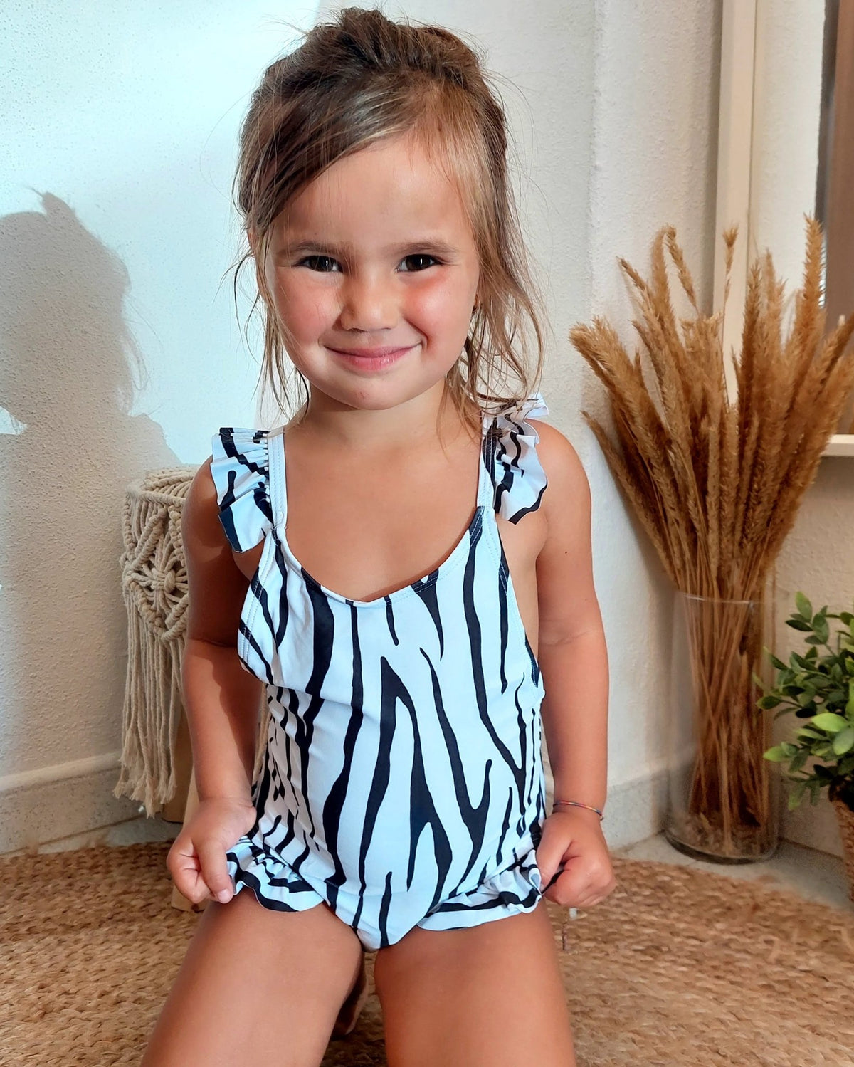 Fato de banho infantil às riscas zebra, com folhos nas alças e decote em V.