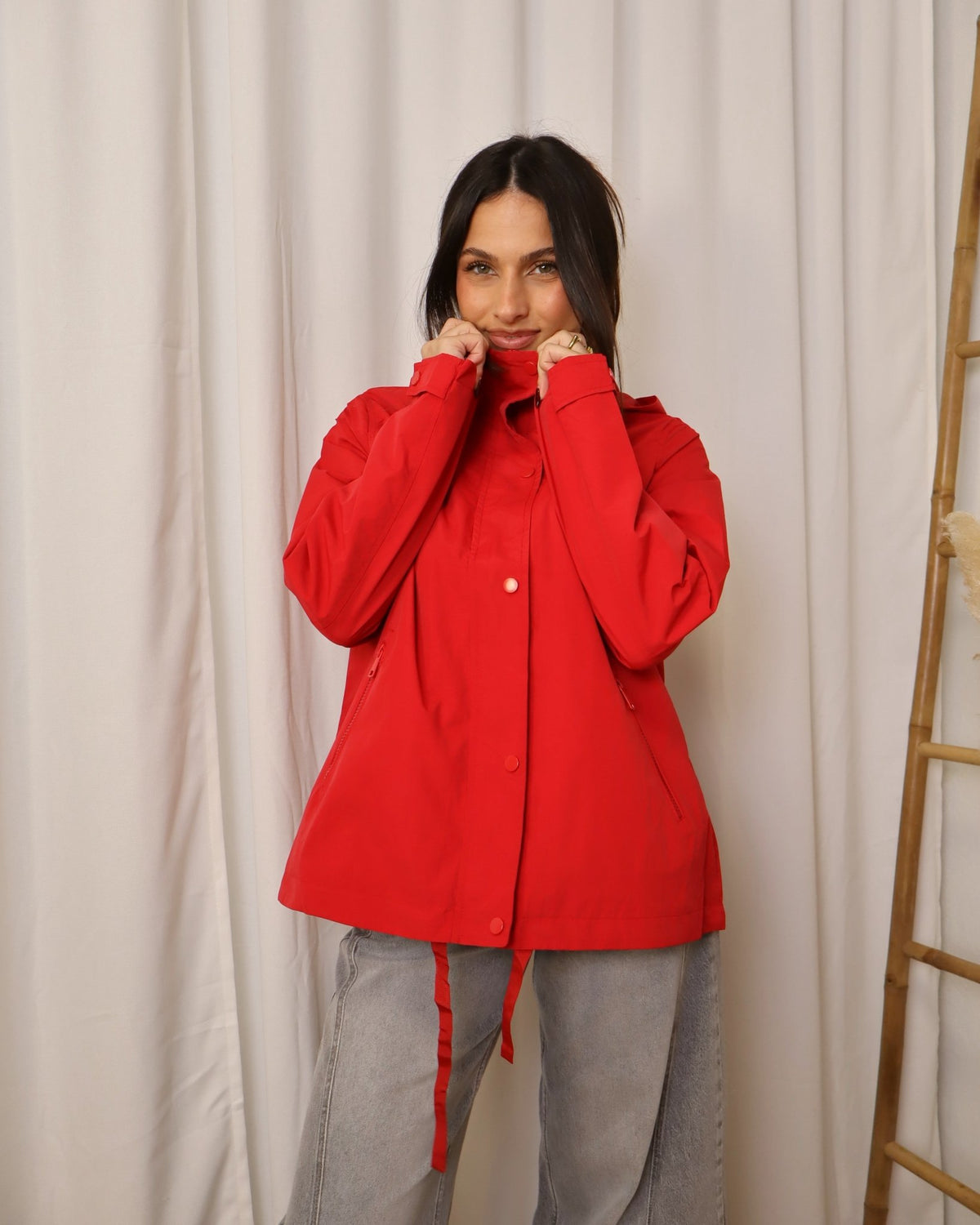 Parka vermelha com capuz, fecho de botões e cordões na cintura, estilo parka.