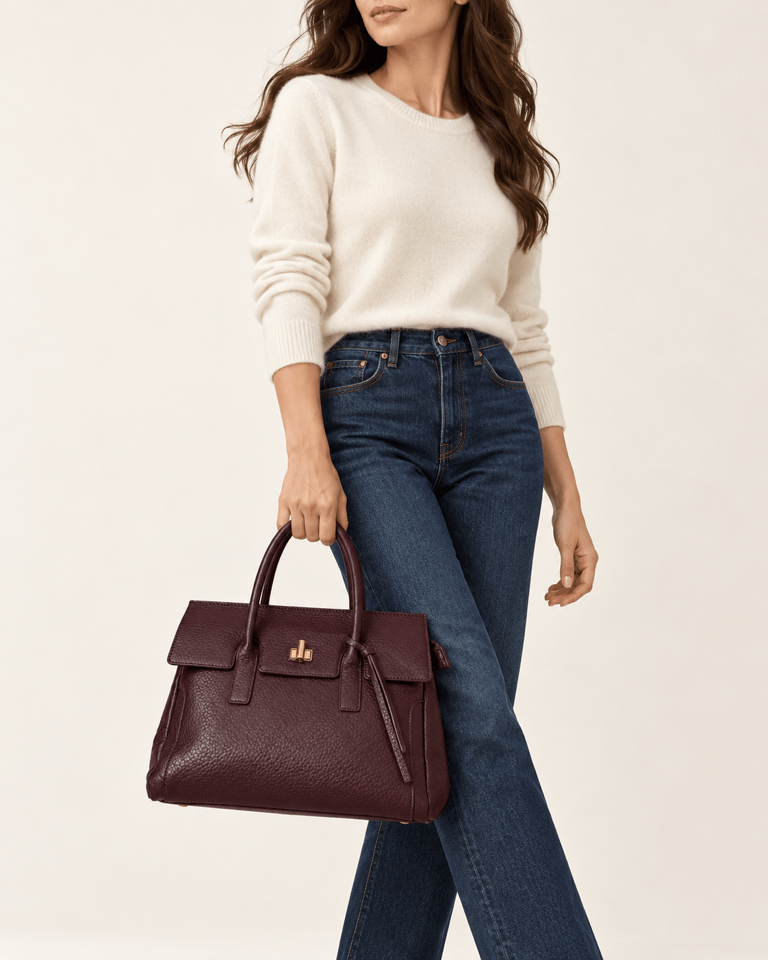 Modelo com camisola clara e calças de ganga a segurar a Mala Júlia bordeaux pelas alças de mão.